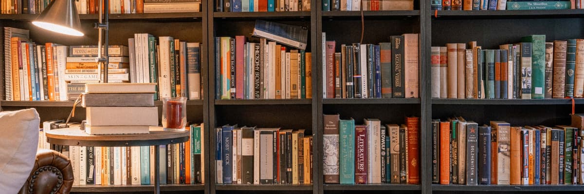 A wall of full bookshelves with a reading lamp and a stack of books on a small round table, the reading behind a counseling psychologist's training.