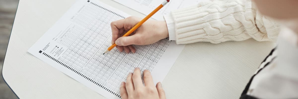 A hand filling in an answer sheet with a pencil at a desk, with a second test booklet beside it, a stand-in for the EPPP.