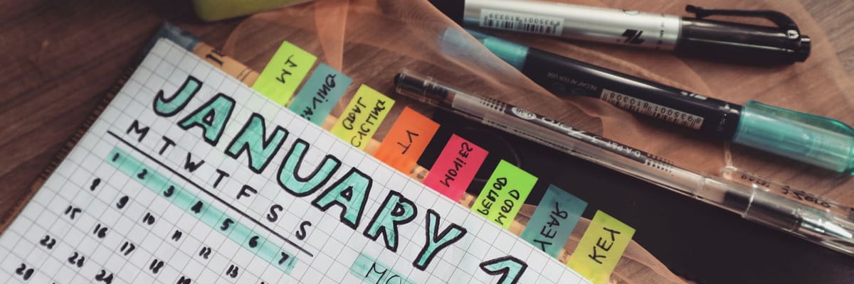 How long is a PsyD program? A hand-lettered weekly planner open to a January calendar, with colored page tabs and pens on a wooden desk.