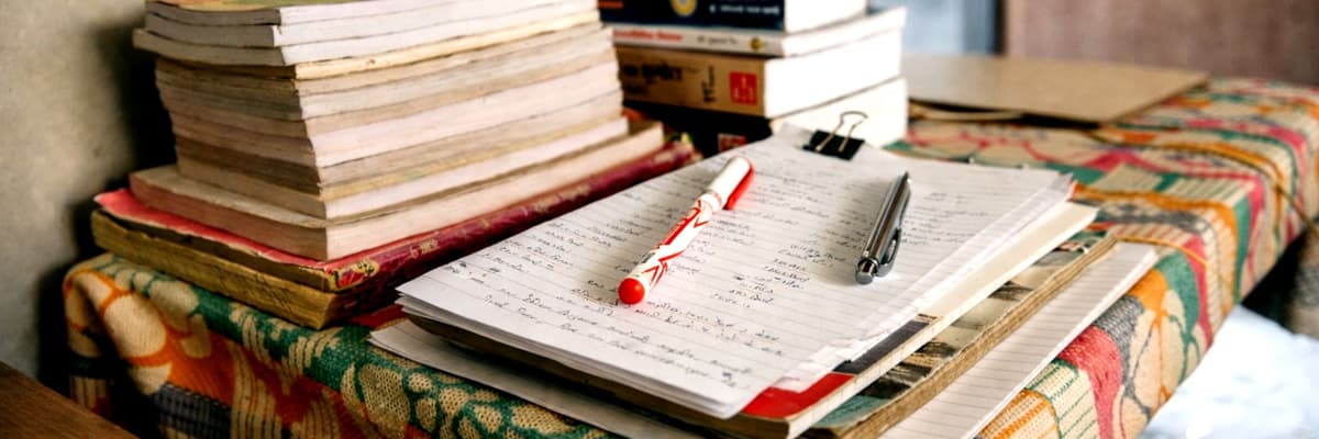 What is a PsyD? It starts at a study desk stacked with books and notebooks, with a handwritten page, a red pen and a binder clip on top.