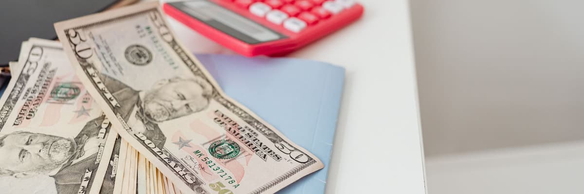 Dollar bills, a pink calculator and notebooks on a white desk, for the cheapest PsyD programs by tuition.