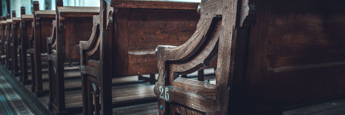Rows of dark wooden church pews in a sunlit interior, for Christian PsyD programs.