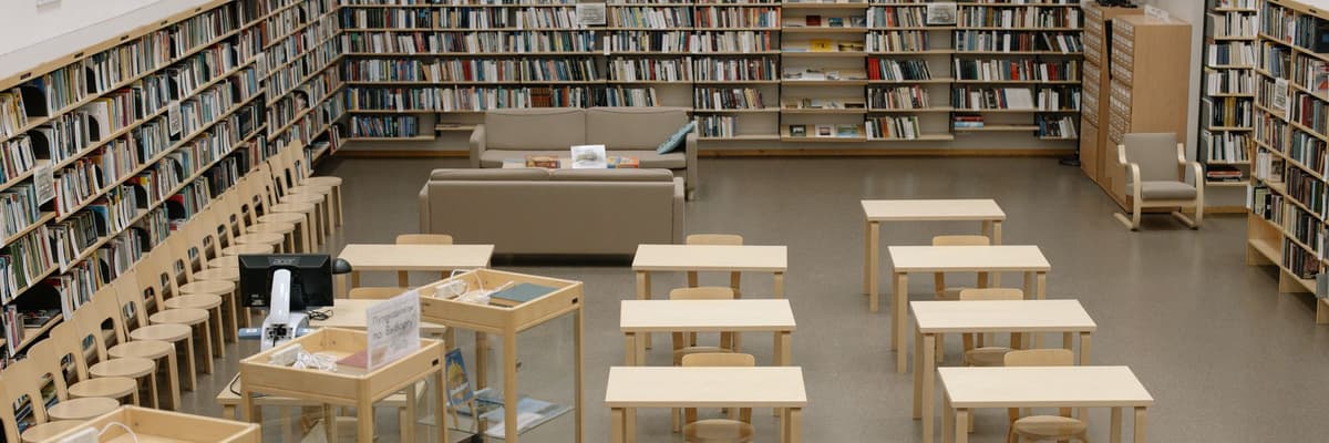A university reading room with low shelves of books along the walls and rows of small wooden study tables, a quiet place to prepare for a PsyD in clinical psychology.