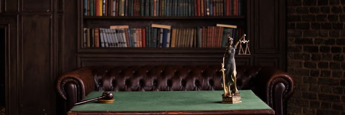 A gavel and a Lady Justice figurine on a green desk in front of a wall of law books, for forensic psychology doctoral programs.