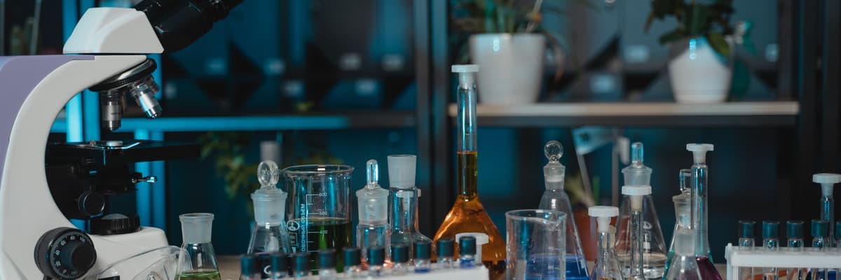 A microscope beside a rack of test tubes and glass flasks on a laboratory shelf, a research setting for neuropsychology doctoral programs.