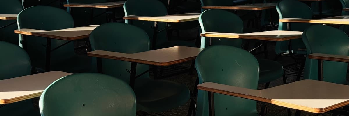 Rows of empty green chairs with wooden writing arms in a sunlit classroom, a school setting for school psychology PsyD programs.