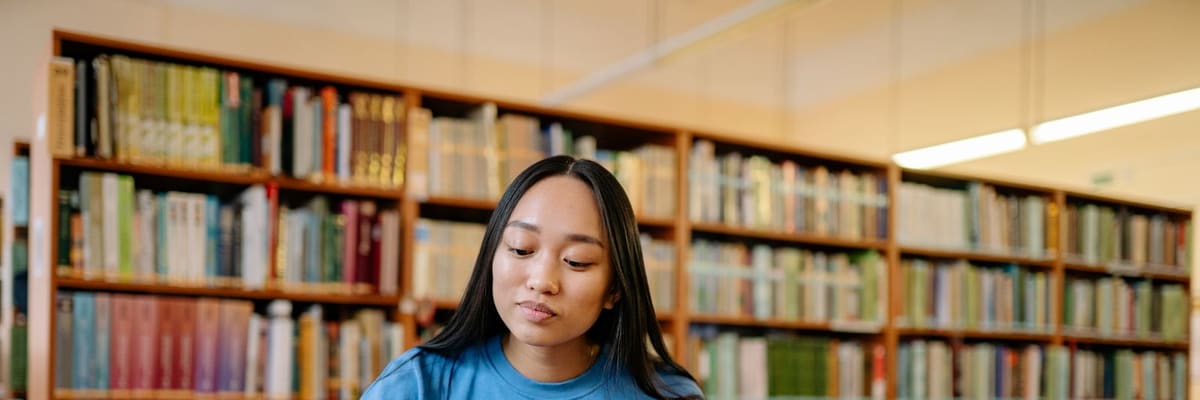 A graduate student studying in front of tall library bookshelves, the training behind a PsyD salary