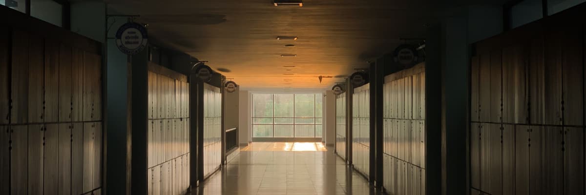 A long empty school corridor lined with lockers, lit by warm evening light from the far end, the setting for a school psychologist salary