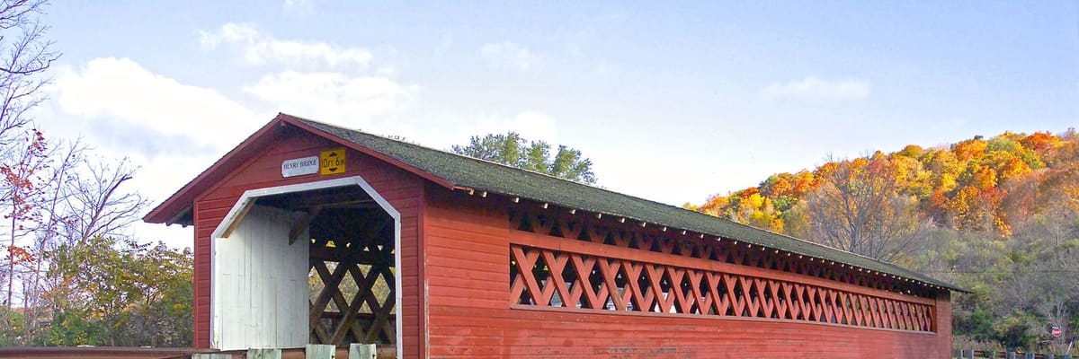 A red covered bridge over a river in Vermont, surrounded by autumn foliage