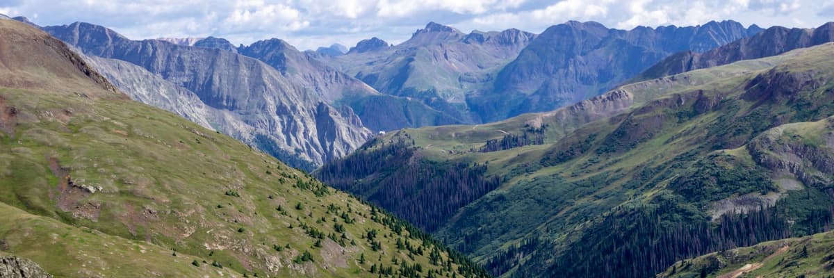 Green alpine slopes and rugged Rocky Mountain peaks beneath cloudy skies at Engineer Pass in Colorado. The photograph opens the ranking of PsyD programs in Colorado.