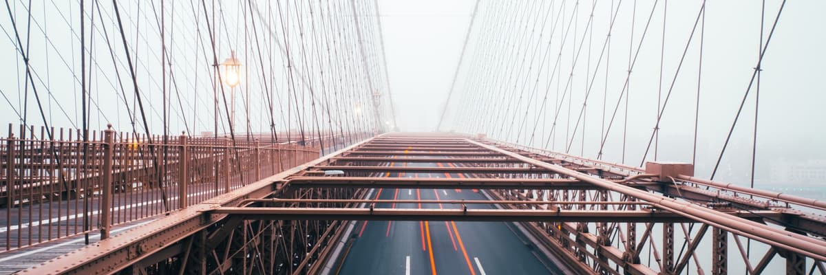 The Brooklyn Bridge in New York on a foggy morning, its roadway and suspension cables fading into the mist. The photograph opens the ranking of PsyD programs in New York.