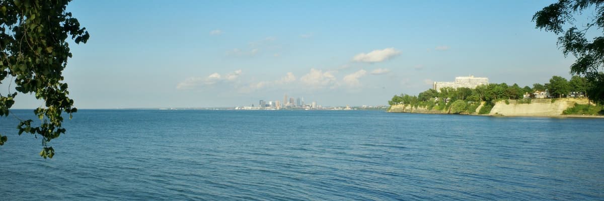 The Cleveland, Ohio skyline on the far shore of Lake Erie, seen across open blue water with a wooded bluff to the right. The photograph opens the ranking of PsyD programs in Ohio.