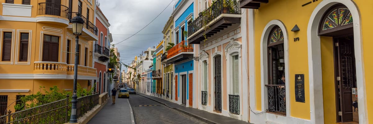 A cobblestone street lined with yellow, blue and pink colonial buildings in Old San Juan, Puerto Rico. The photograph opens the ranking of PsyD programs in Puerto Rico.
