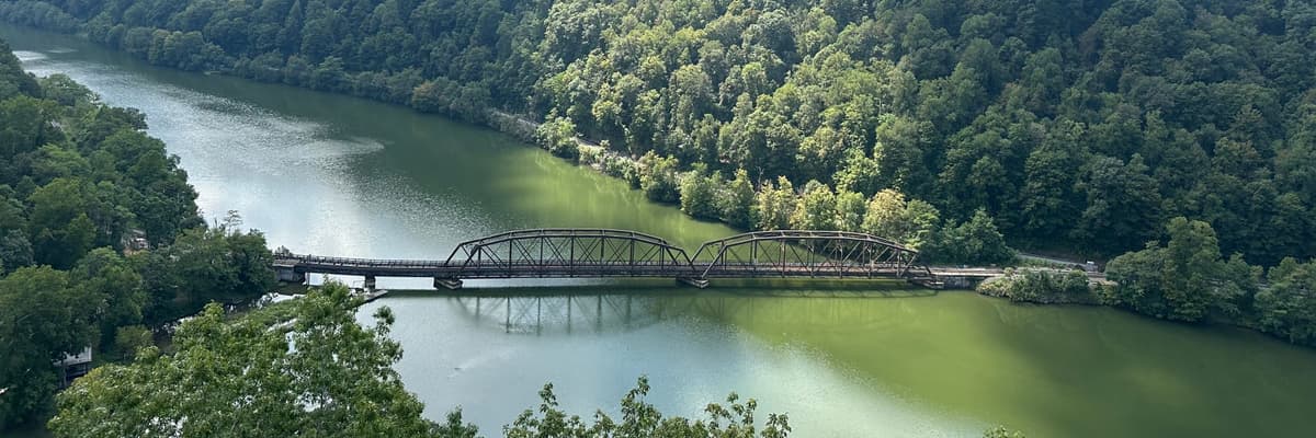 A steel truss bridge over a green river below forested hills in the New River Gorge area of West Virginia. The photograph opens the ranking of PsyD programs in West Virginia.