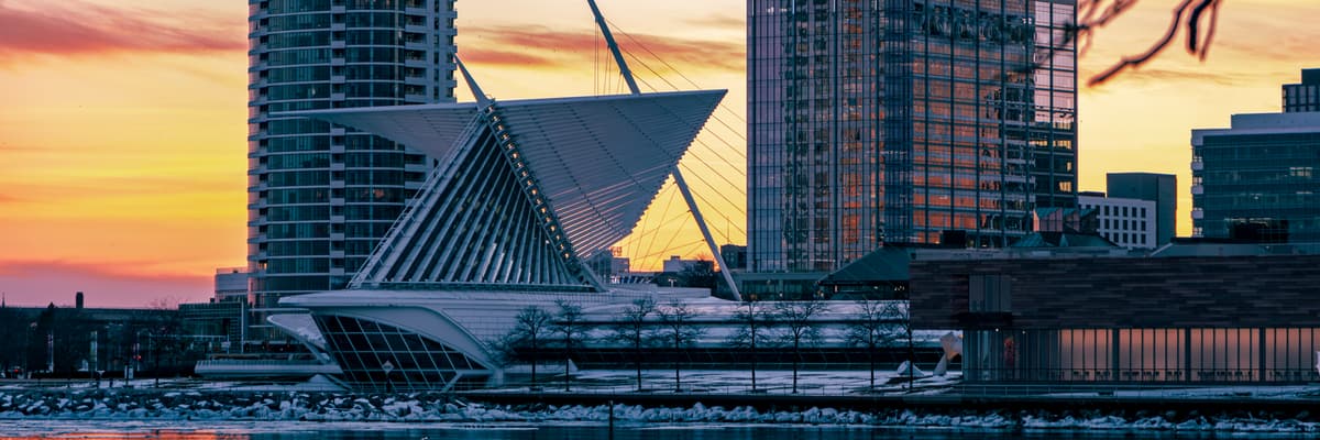 The winged Milwaukee Art Museum pavilion and downtown towers against an orange sunset sky on the Lake Michigan shore in Milwaukee, Wisconsin. The photograph opens the ranking of PsyD programs in Wisconsin.