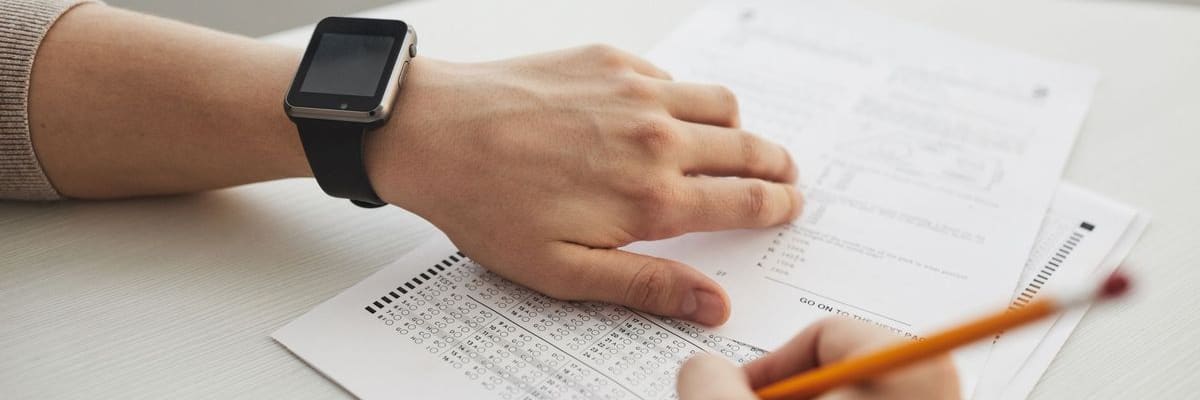 EPPP results start with an answer sheet: a hand resting on a multiple-choice answer sheet, with a smartwatch on the wrist and an orange pencil held below.