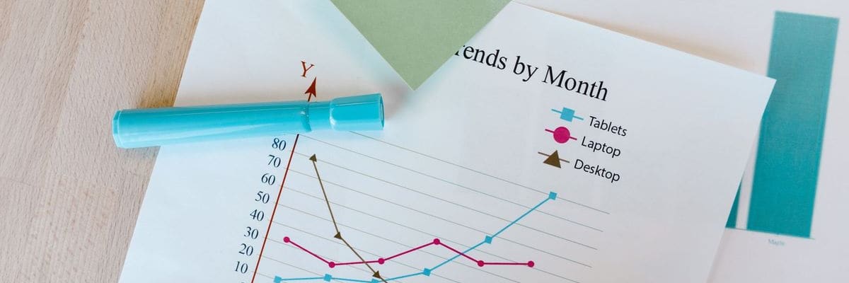 A printed line chart of trends by month on a wooden desk, with a blue marker lying across its axis.