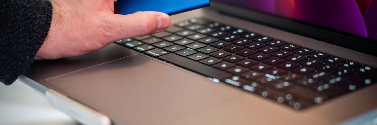 A hand holding a small blue drive just above the keyboard of an open laptop.